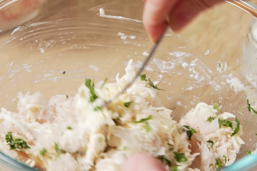 En un cuenco, añadimos 350 g de merluza picada (puede ser con picadora), 150 g de mozzarella rallada, 100 g de queso crema, sal, pimienta, ½ cdta. de ajo en polvo y 1 cdta. de perejil picado. Mezclamos con una lengua o pala hasta conseguir una masa.