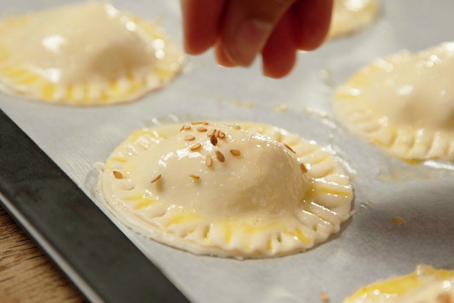 Receta casera de Mini empanadas de bacalao. Pincelamos las empanadillas con huevo batido, les añadimos sésamo por encima y las horneamos 12 minutos a 200º.