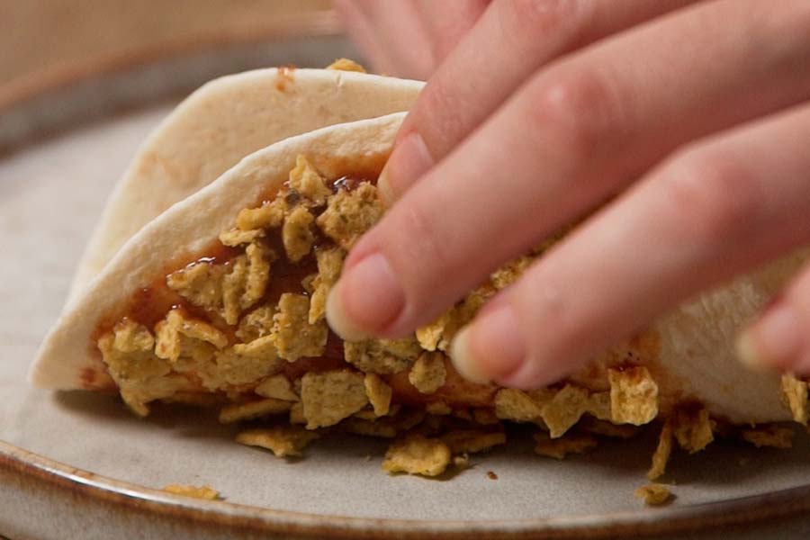 Receta casera de Tacos crujientes de carne. Preparamos los tacos mojando tortitas de trigo en salsa barbacoa Doctor Salsas y pasándolas por nachos triturados. Las plegamos dando forma de taco y sujetamos con palillos para que conserven la forma. Horneamos 5 minutos a 200º.