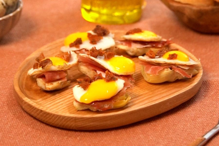 Receta casera de Alcachofas con jamón y huevo de codorniz. Montamos las alcachofas añadiendo el huevo de codorniz, jamón serrano y tomate seco en aceite troceado